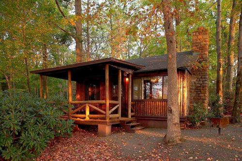 A cozy wooden cabin surrounded by trees and autumn foliage, featuring a porch and stone chimney.