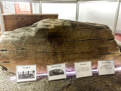 A large rock display with four framed illustrations labeled Portuguese, American Indian, Phoenician, and Norse or Viking.