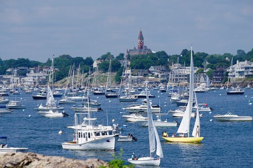 A busy harbor filled with sailboats and motorboats, with a church steeple visible in the background.