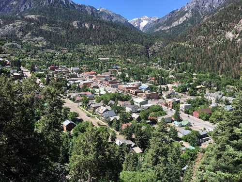 Aerial view of a small town nestled in a valley, surrounded by mountains and lush greenery under a clear blue sky.