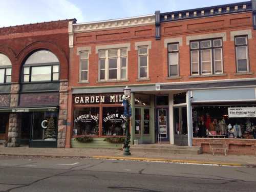 Historic brick buildings line a street, featuring shops like "Garden Mill" and "The Potting Nest."