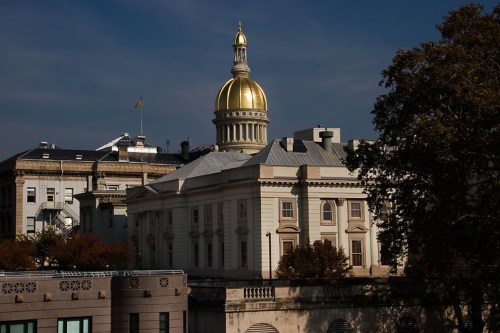 The New Jersey State House with a golden dome, surrounded by trees and a clear blue sky.