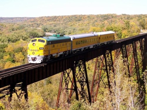 A vintage train crosses a tall bridge surrounded by colorful autumn trees.