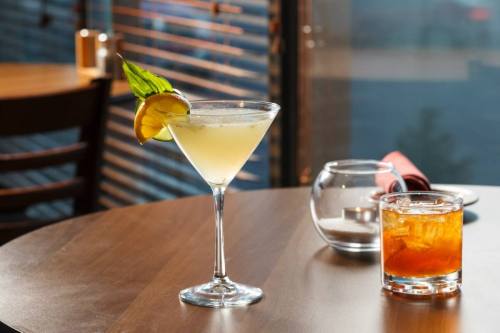 A refreshing cocktail in a martini glass with a lemon slice, alongside a glass of whiskey on a wooden table.