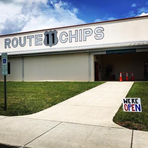 A building with "Route 11 Chips" sign, a clear sky, and a "We're Open" sign on the sidewalk.