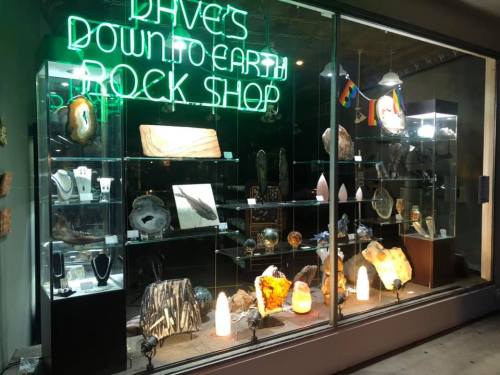 A brightly lit rock shop window displays various crystals and stones, with a neon sign reading "Dave's Down to Earth."