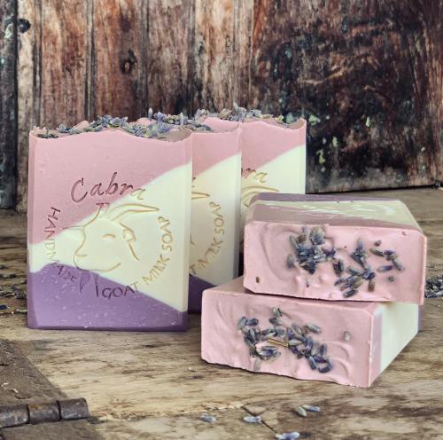 Three bars of lavender soap with a goat design, featuring pink and cream swirls, placed on a rustic wooden surface.