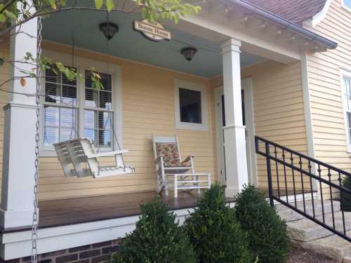 A cozy porch with a swing, rocking chair, and neatly trimmed bushes on a sunny day.