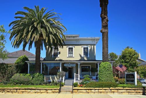 A charming two-story house with palm trees, a front porch, and an American flag, set against a clear blue sky.