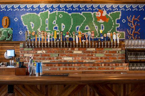 A bar with a brick wall, featuring a colorful mosaic and a row of beer taps on the counter.
