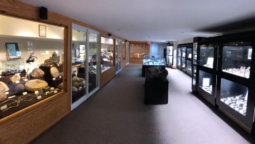 A spacious museum exhibit featuring display cases filled with various rocks and minerals along a well-lit corridor.
