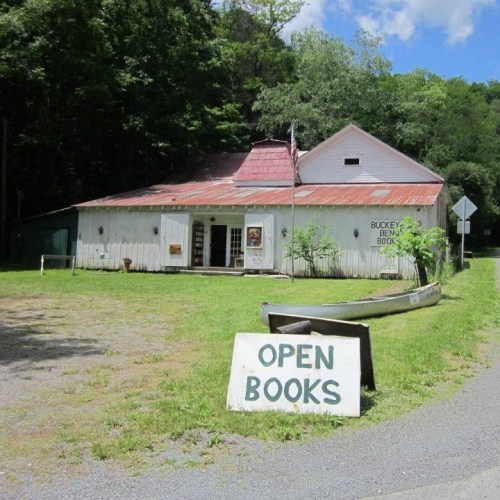 A rustic bookstore with a sign reading "OPEN BOOKS," surrounded by trees and a gravel path.