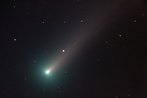 A bright comet with a glowing green head and a long, faint tail, surrounded by stars in a dark night sky.