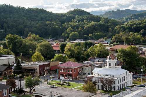 A scenic view of a small town surrounded by green hills, featuring historic buildings and a courthouse.