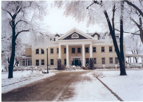 A large, elegant house surrounded by snow-covered trees and a frosty landscape, creating a serene winter scene.