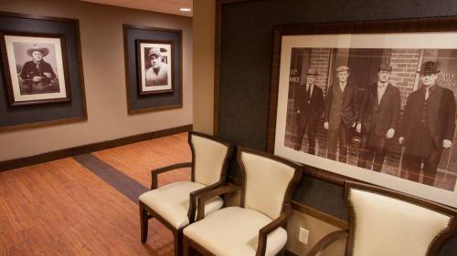 A hallway with framed black-and-white photos of men in suits and two empty chairs against a wooden floor.