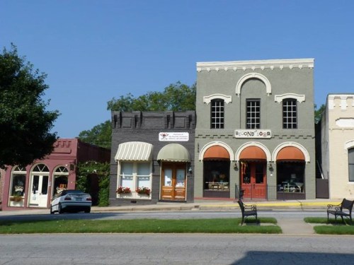 A charming street scene featuring colorful storefronts and a parked car under a clear blue sky.
