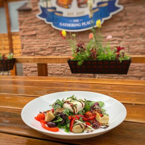 A fresh salad with mixed greens, cherry tomatoes, and edible flowers, served on a wooden table outdoors.