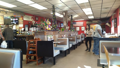 A cozy restaurant interior with booths, festive decorations, and a counter. A server walks by, and customers are seated.