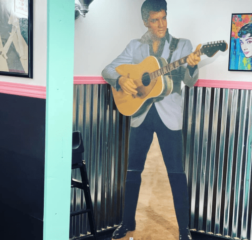 A life-sized cutout of a man in a blue suit playing guitar, set against a colorful diner backdrop.