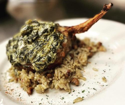 A plate featuring a cooked chop topped with green sauce, served over seasoned rice with herbs and spices.