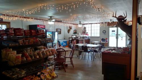 Cozy store interior decorated with lights, featuring snacks, tables, and a deer mount, with a Christmas tree in the corner.