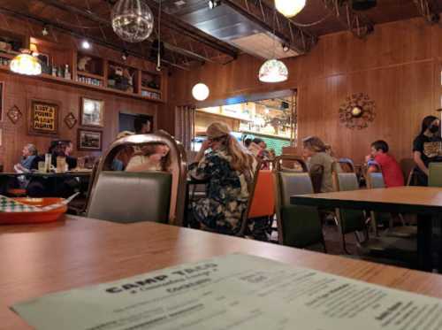 A cozy restaurant interior with wooden walls, colorful chairs, and patrons enjoying their meals at various tables.