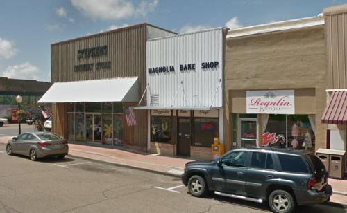 A street view of shops, including Magnolia Bake Shop, with parked cars and blue skies above.