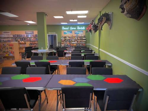 A spacious board game store with tables set up for play, shelves filled with games, and colorful decorations on the walls.