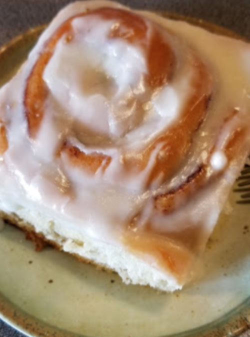 A close-up of a cinnamon roll topped with white icing on a decorative plate.