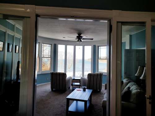 A cozy living room with two striped chairs and a coffee table, overlooking a scenic view of the water through large windows.