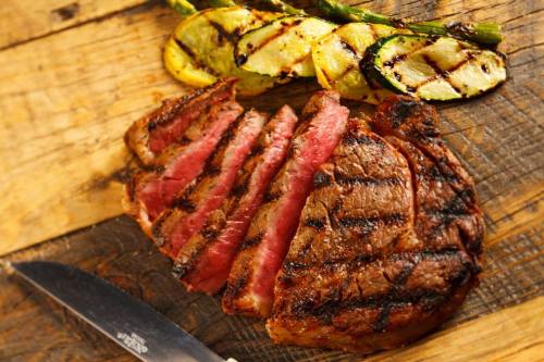 Grilled steak sliced on a wooden board, accompanied by grilled zucchini and asparagus.