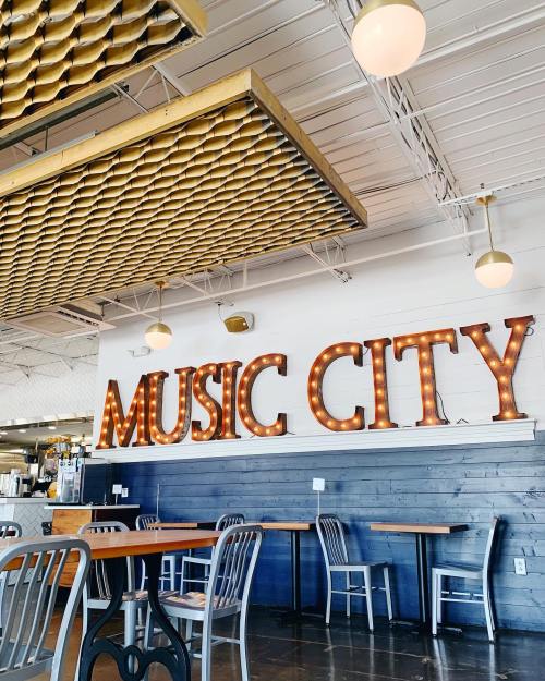 Interior of a cafe featuring a "MUSIC CITY" sign with lights, wooden tables, and modern decor.