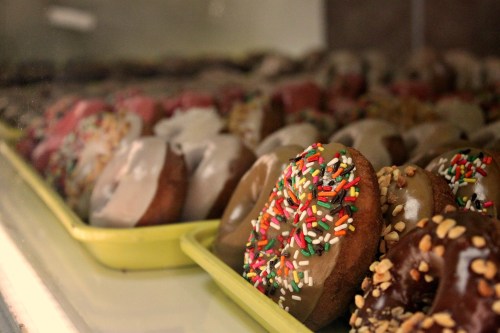 A display of colorful donuts with various toppings, including sprinkles and chocolate glaze, in a bakery case.