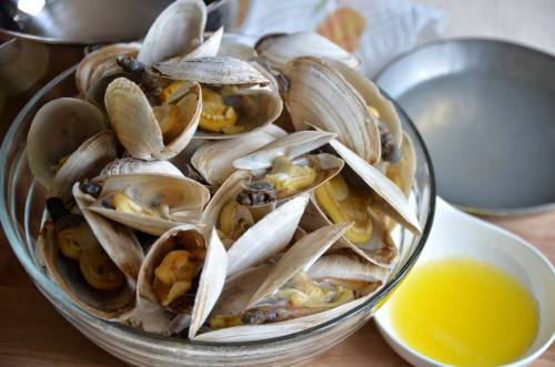 A glass bowl filled with fresh clams, with a small dish of melted butter nearby.