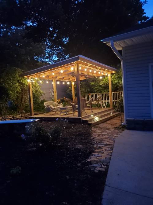 A cozy outdoor patio with string lights, surrounded by greenery, creating a warm evening atmosphere.