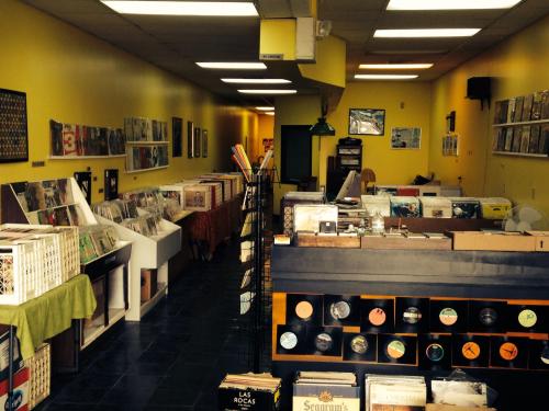 A cozy record store with yellow walls, shelves of vinyl records, and a welcoming atmosphere.