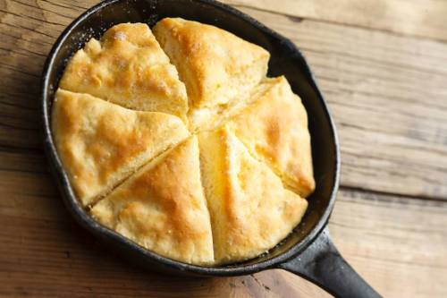 A freshly baked cornbread, cut into wedges, in a cast iron skillet on a wooden surface.