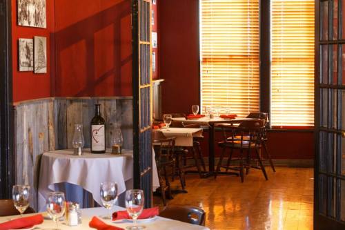 Cozy restaurant interior with wooden tables, red accents, and wine bottles, featuring warm lighting and a welcoming atmosphere.