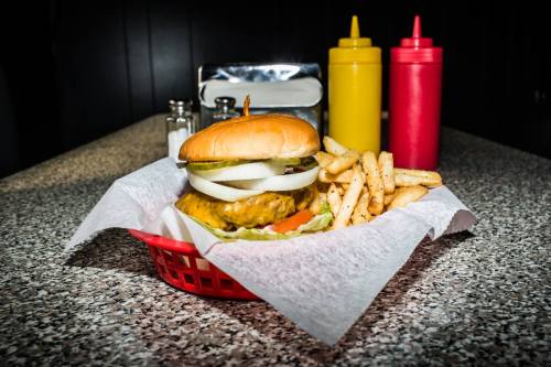 A juicy burger with lettuce, tomato, and onion, served with fries in a red basket, alongside mustard and ketchup bottles.