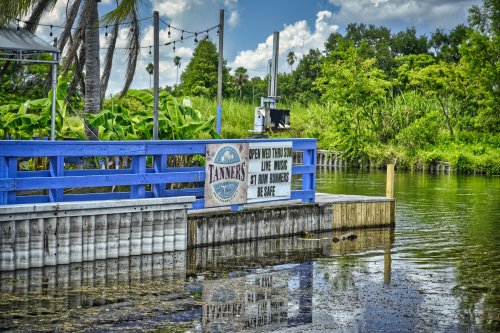 A blue dock with a sign for Tanners, surrounded by greenery and water under a bright sky.