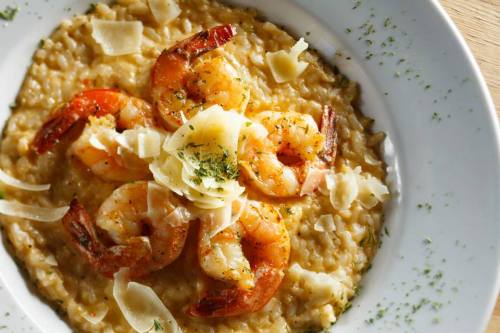 Creamy risotto topped with grilled shrimp and shaved cheese, garnished with herbs on a white plate.