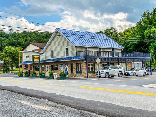 A two-story building with a blue roof, surrounded by greenery, featuring a sign and parked cars on a quiet street.
