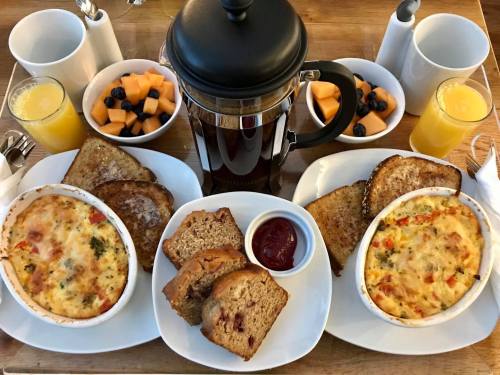 A breakfast spread featuring baked egg dishes, toast, fruit cups, and coffee on a wooden tray.