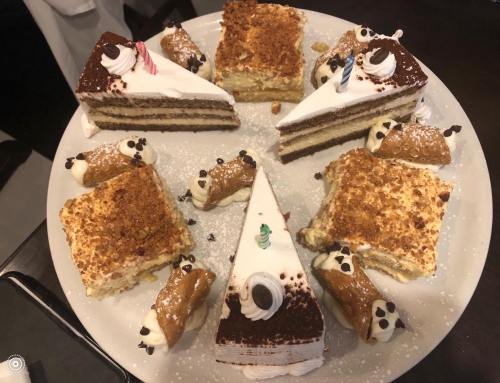 A plate of assorted desserts featuring layered cakes and mini cannoli, decorated with cream and chocolate accents.