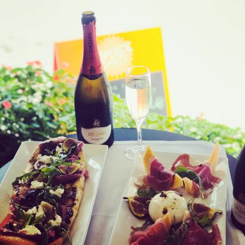 A table setting with two gourmet dishes, a glass of sparkling wine, and a bottle of champagne, surrounded by greenery.