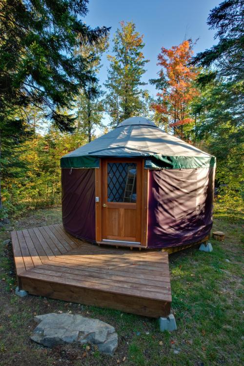 A cozy yurt with a wooden deck, surrounded by trees and autumn foliage.