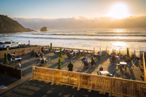 Outdoor dining area by the beach at sunset, with people seated and waves crashing in the background.