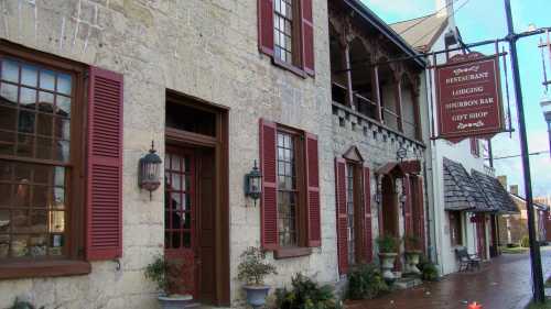 Historic building with red shutters, featuring a restaurant, lodging, and gift shop sign. Cobblestone path in front.