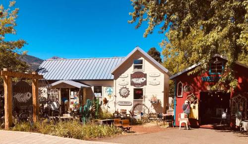 Colorful storefronts with unique signs and decorations, surrounded by trees and a clear blue sky.